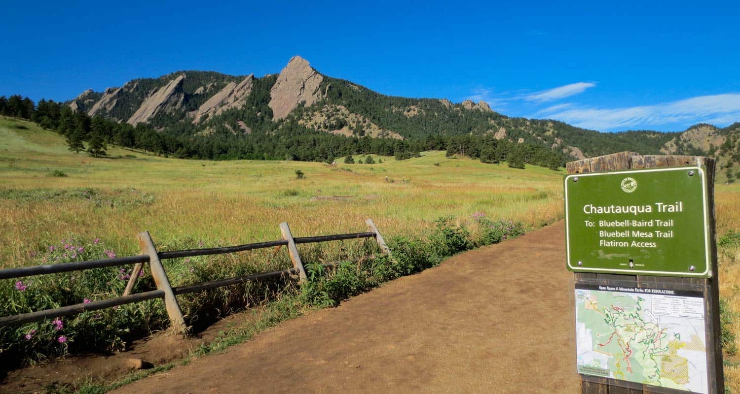 dirt trail leading toward the flatirons of boulder colorado in chautauqua park wooden fence in foreground and broad meadows