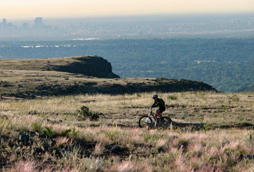 mountain biker on top of north table mountain with denver skyline in background
