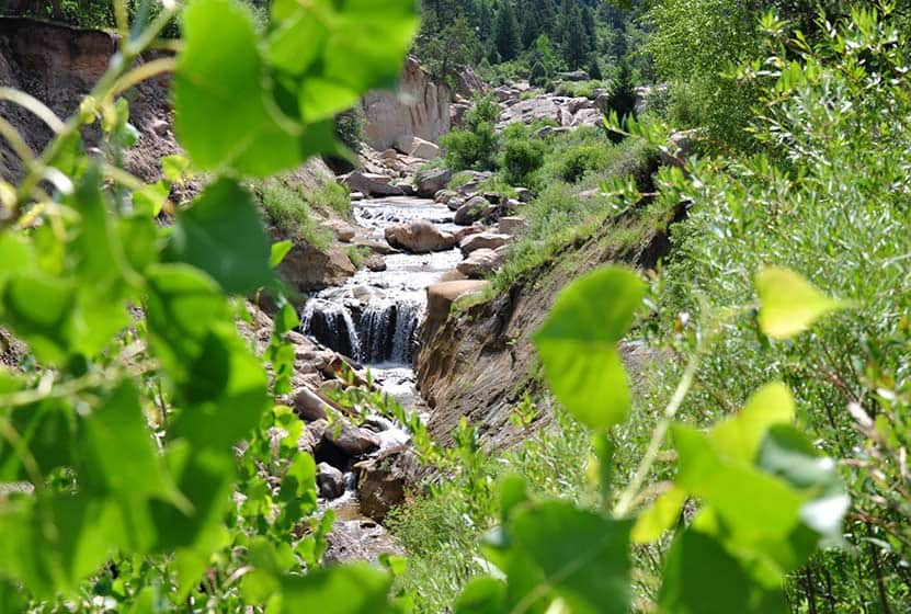 cherry creek waterfall flowing through Castlewood Canyon State Park with cottonwood leaves in foreground on hike near denver colorado