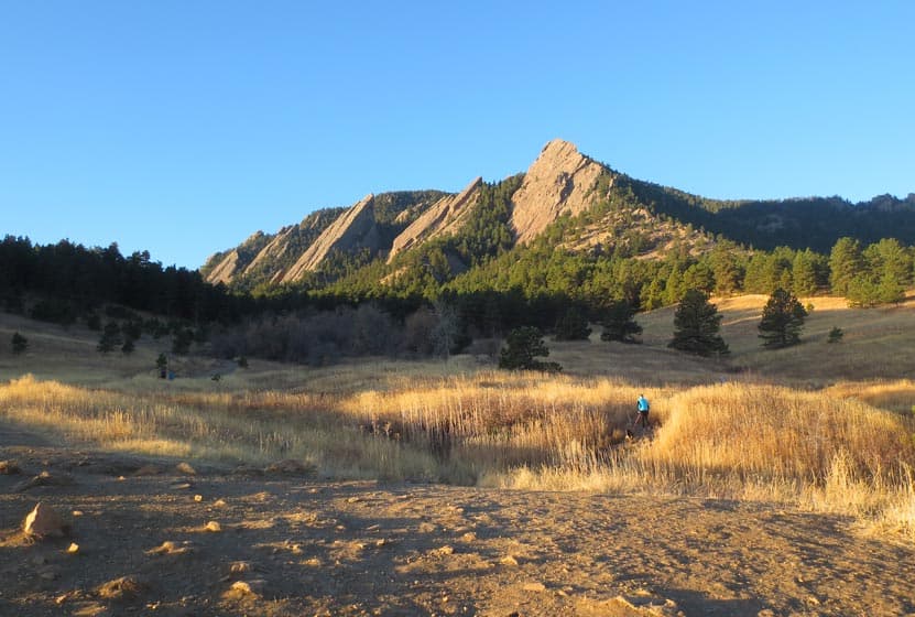 hiker in foreground on trail near Denver at chautauqua park with flatirons mountains in background and blue sky near denver