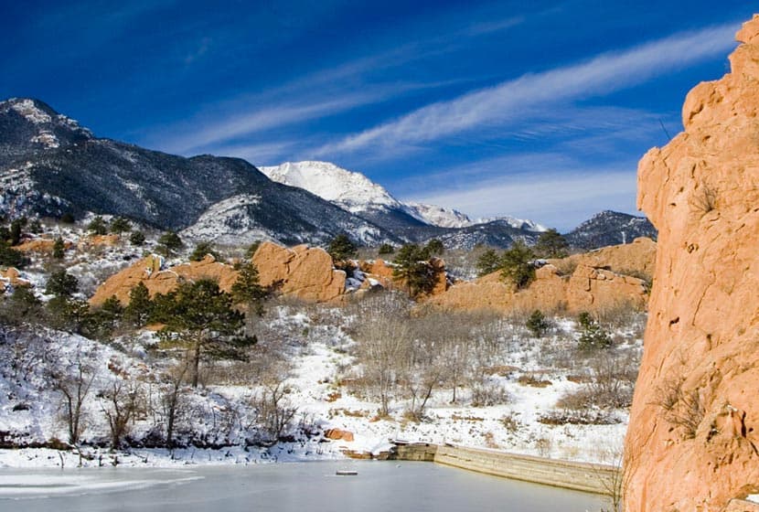 quarry pond in foreground and red rock formations on snowy afternoon with pikes peak in background on hike at red rock canyon open space in colorado springs