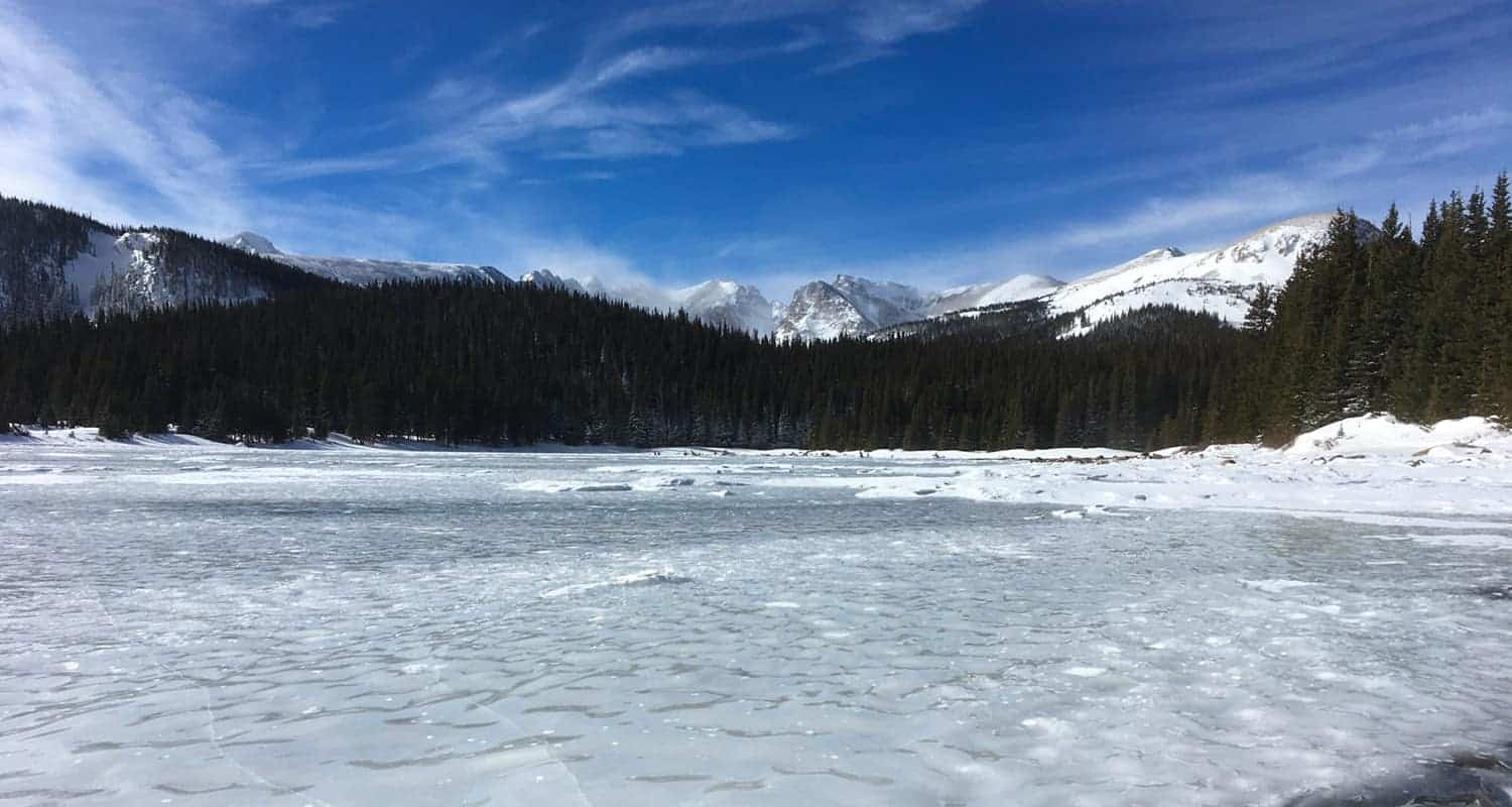 frozen brainard lake with snowcapped mountains in background on hike along waldrop trail to cmc cabin