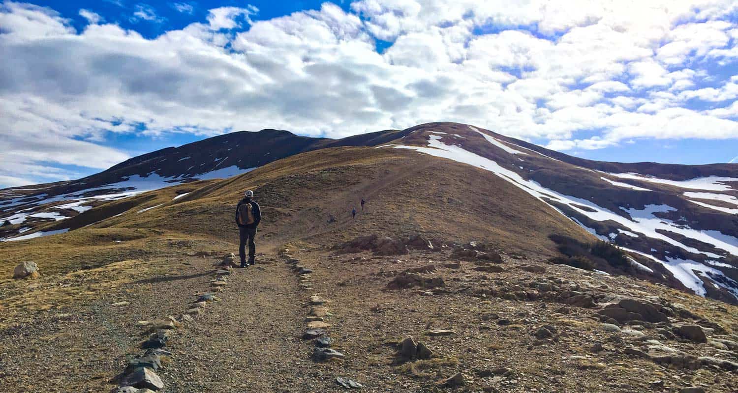 hiker at the beginning of the sniktau and grizzly trail on loveland pass with tundra of mountains in foreground and blue skies with clouds on hiike near denver