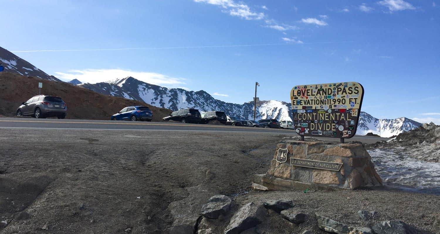 loveland pass trailhead with USFS sign with stickers on it and cars with mountains in background