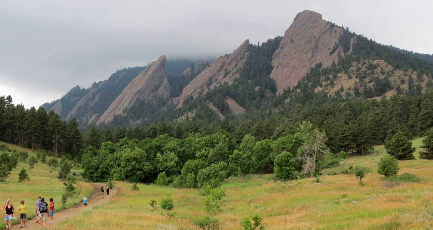 view of the flatirons in boulders chatauqua park with meadow in foreground and fog lifting