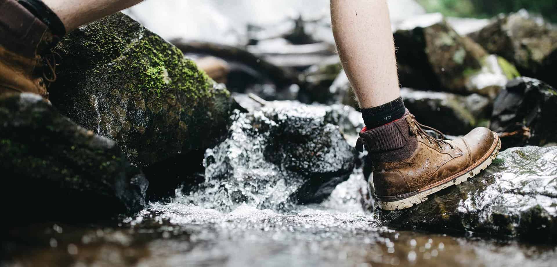 man hiking through water on rocks wearing hiking boots